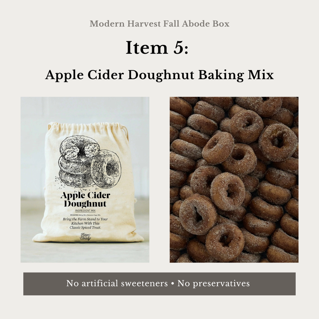Promotional graphic for Modern Harvest Fall Abode Box's Apple Cider Doughnut Baking Mix. The image features a cream-colored drawstring bag with a black graphic of doughnuts and the product name, next to a close-up photo of a pile of baked apple cider doughnuts dusted with sugar.