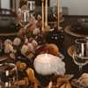 Decorative table setting with candles, glasses, and leaves on a dark surface.