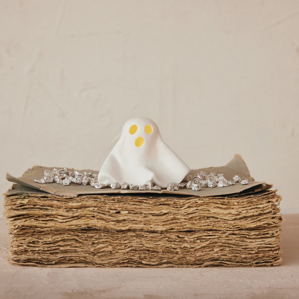 White ghost figurine on a stack of brown paper with a beige background