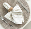 Table setting with woven placemat, striped napkin, and cutlery on a neutral background
