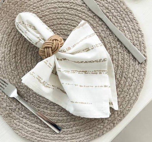 Table setting with woven placemat, striped napkin, and cutlery on a neutral background