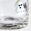 A close-up of a clear glass tumbler with a small white ghost decoration featuring black eyes on the side.