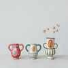 A set of three hand-painted ceramic bud vases in different colors, with the top vase being pinkish-red with blue details, the middle vase being green with blue details, and the bottom vase being a solid green. Each vase has a handle and is adorned with floral hand-painted designs.