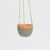 Hanging ceramic planter with a gray body and brown top on a light gray background
