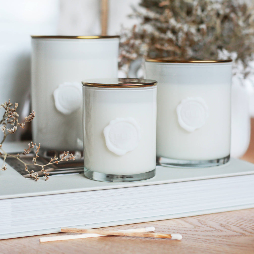 Three white candles with gold rims on a wooden surface with dried plants.