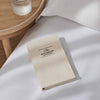 Beige notebook titled 'The Five Minute Journal' on a white surface with a wooden side table in the background.