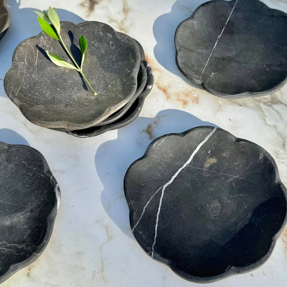 Black marble catchall tray with a green leaf on a marble surface