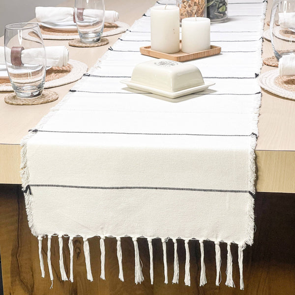 Table setting with a white table runner, glasses, and candles on a wooden table.