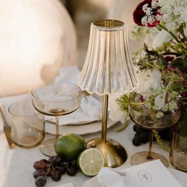 Decorative table setting with gold lamp, glasses, and flowers.