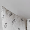 A close-up of a light beige linen throw pillow with a delicate black botanical leaf pattern, shown against a neutral light gray background.