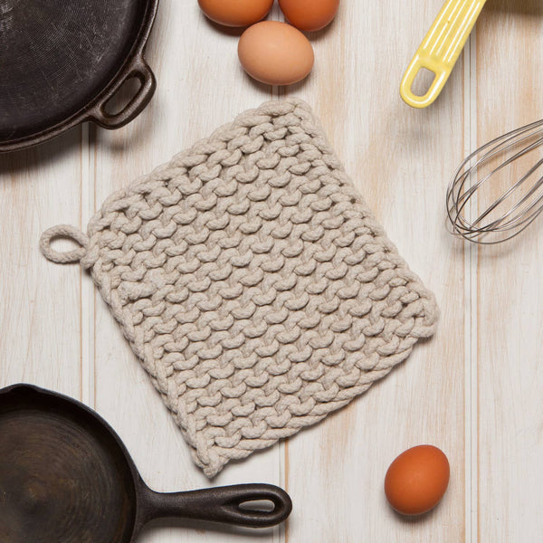 Textured pot holder on a wooden surface with eggs and a whisk.