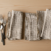 Set of light grey napkins on a wooden surface with cutlery.