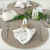Table setting with woven placemats, white napkins, and silverware on a neutral background.