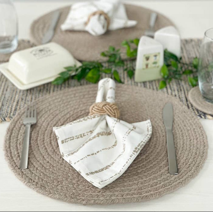 Table setting with woven placemats, white napkins, and silverware on a neutral background.