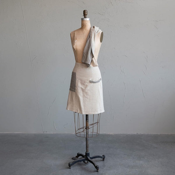 Mannequin wearing a linen and black half apron on a gray background