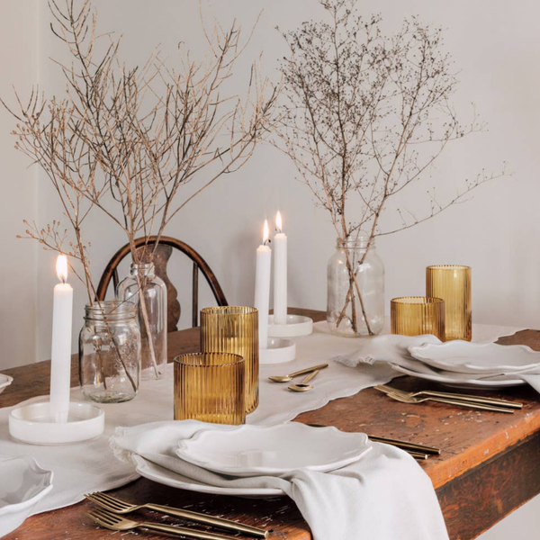 Elegant table setting with table runner, candles, gold and white decor on a wooden table.