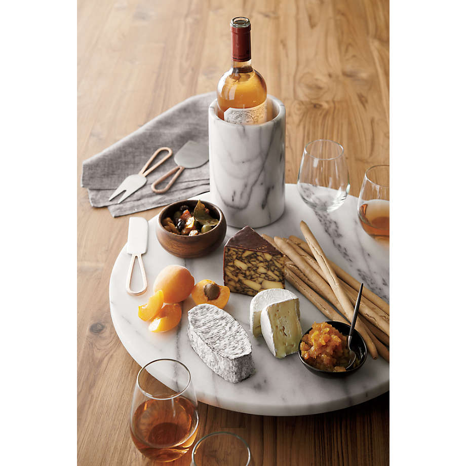 Marble cheeseboard with assorted cheeses, fruits, and a bottle of wine on a wooden table.