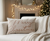 Merry Christmas Lumbar Throw Pillow on white sofa with throw blanket and christmas tree with twinkle lights in the background