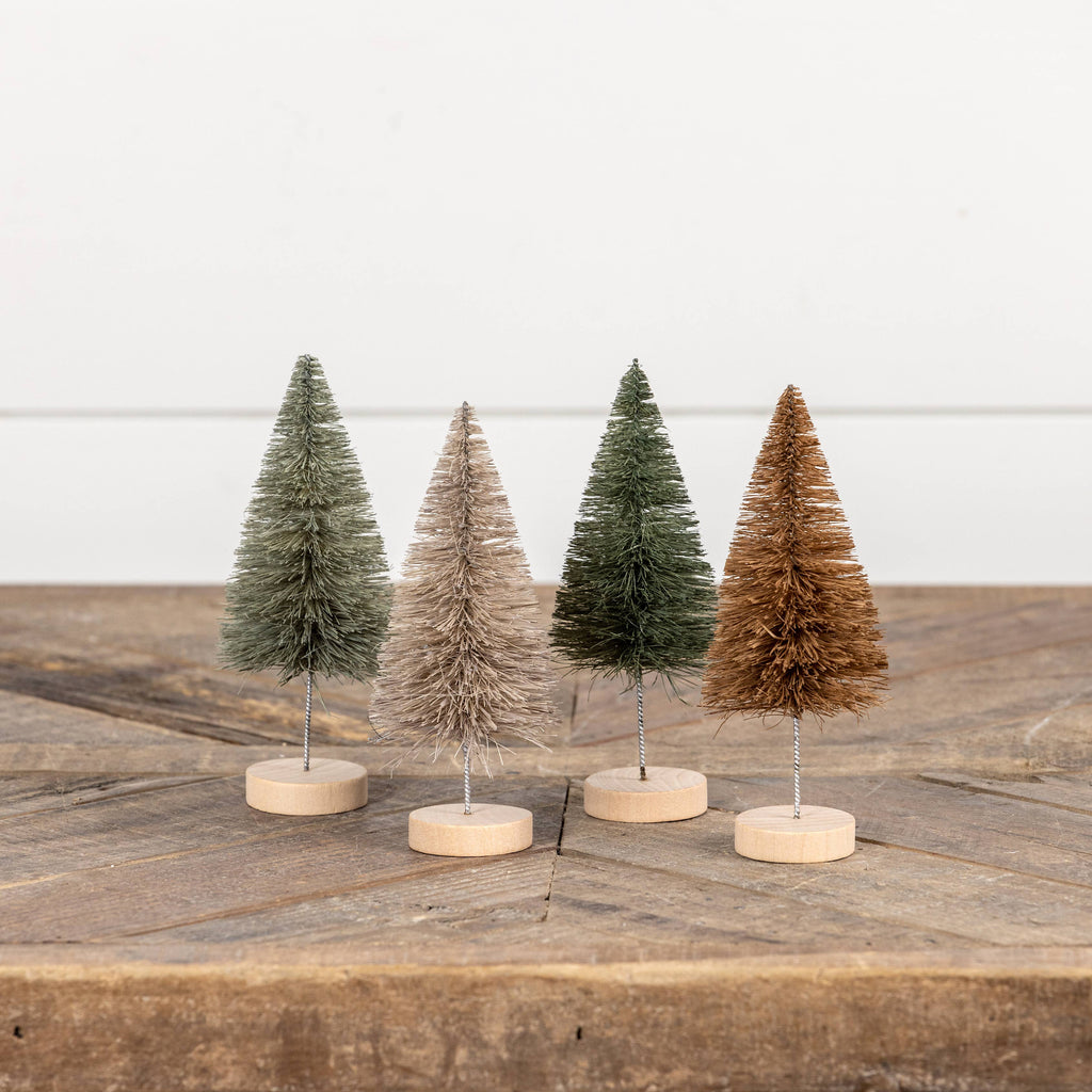 Four small bottle brush Christmas trees on wooden stands against a white background