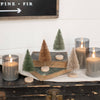 Decorative setup with candles and Neutral Bottle Brush Trees on a wooden surface.