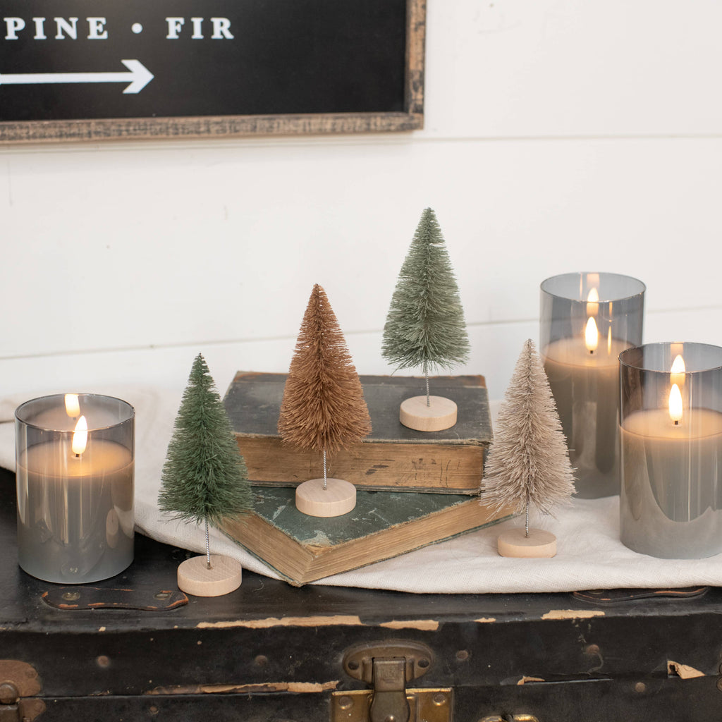 Decorative setup with candles and Neutral Bottle Brush Trees on a wooden surface.
