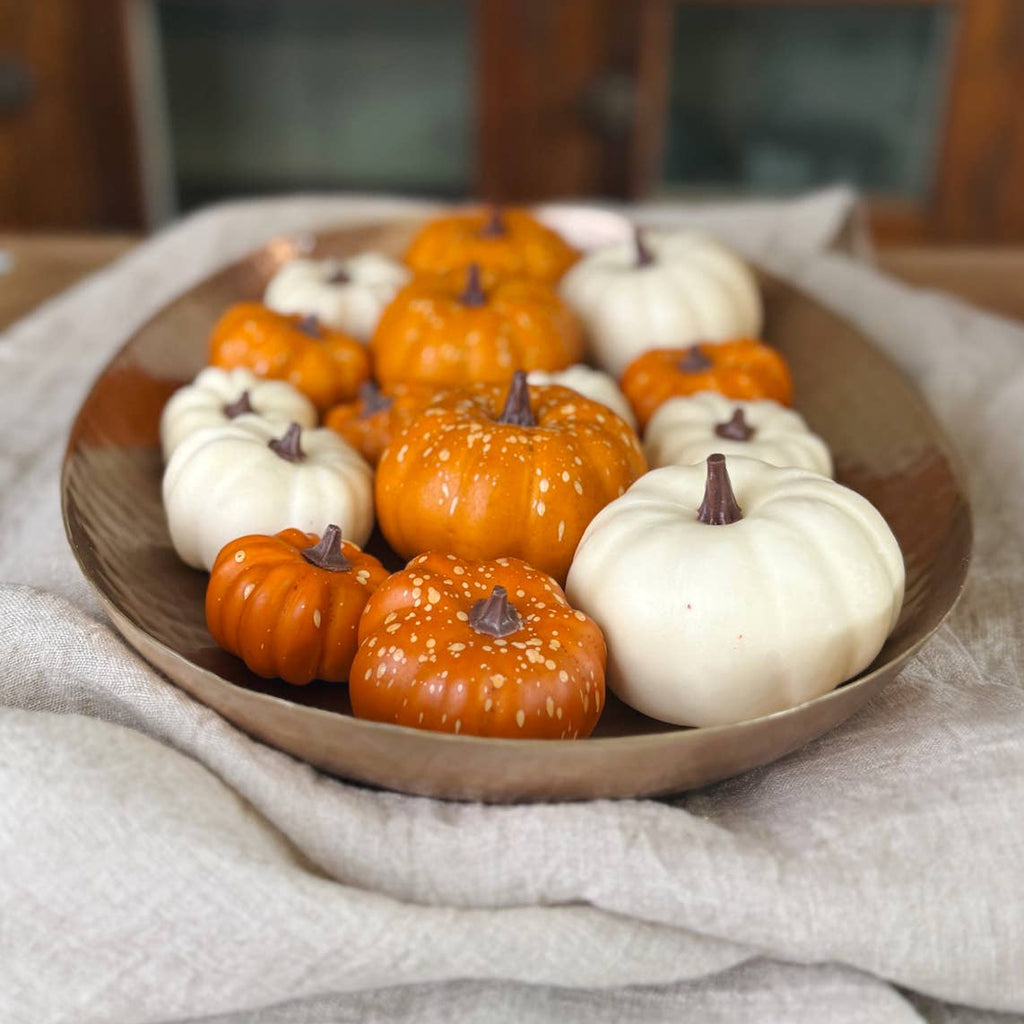 Decorative pumpkins in orange and white on a brass tray with a neutral background