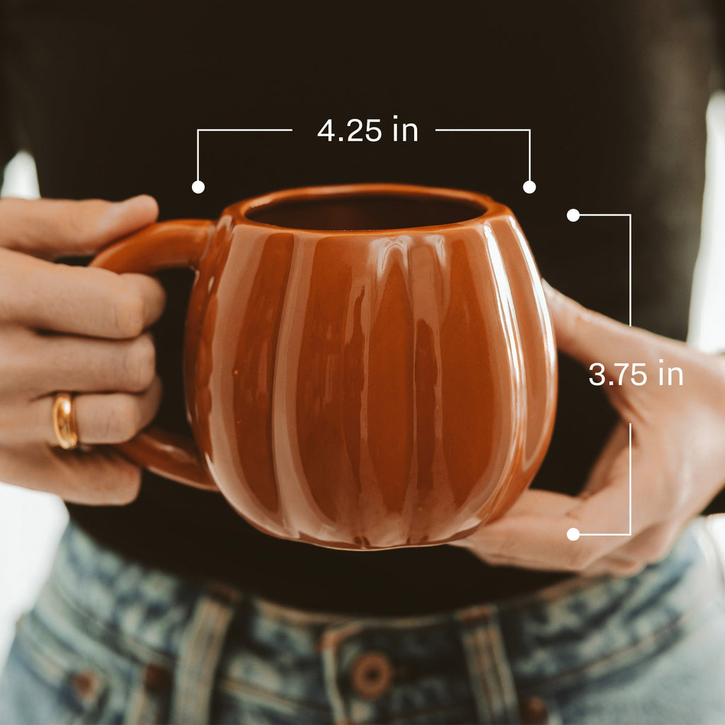 Brown ceramic mug held by hands with measurements indicated, blurred background