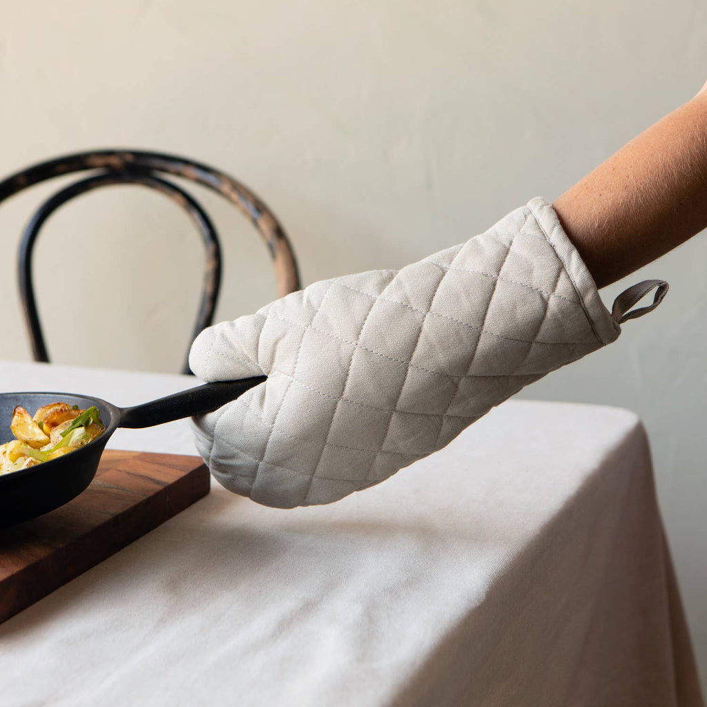 Person wearing an oven mitt holding a pan with food on a table.