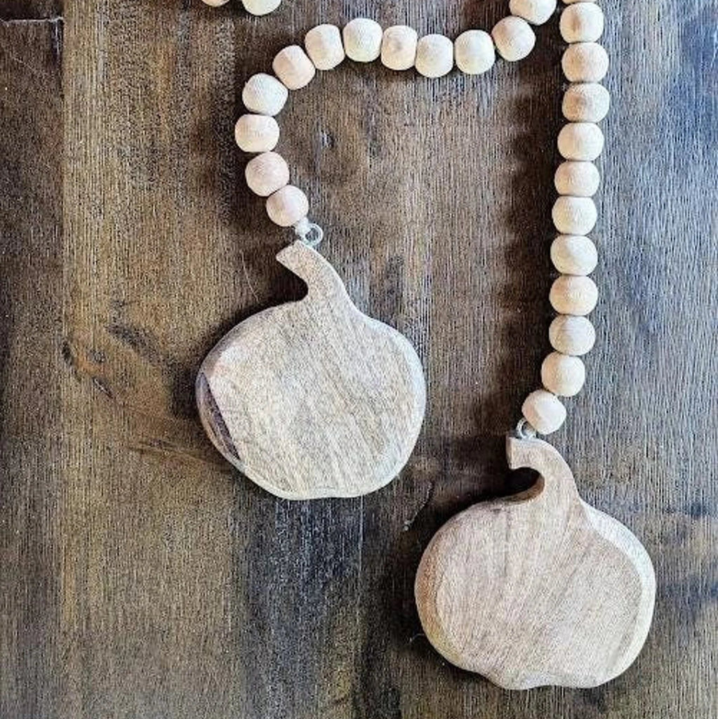 Wooden beaded garland with two large pumpkin elements on a wooden background_rustic fall decor