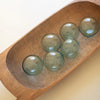 Five green glass balls on a wooden tray with a plain background