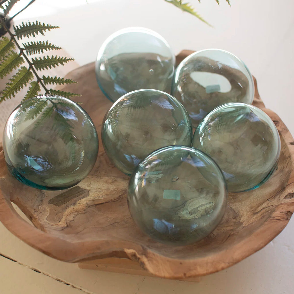 Five transparent glass decorative balls on a wooden tray with a plant in the background