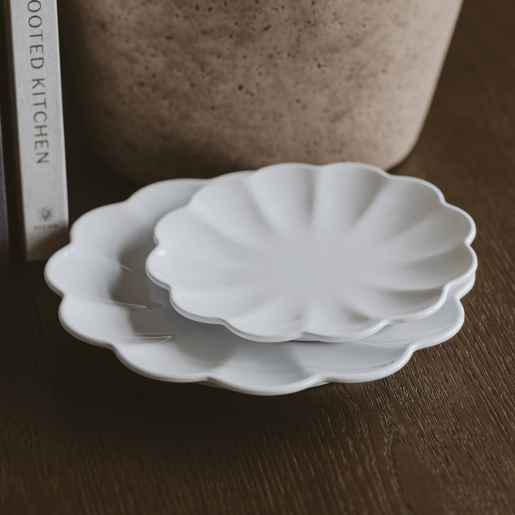 Two white melamine trays with scalloped edges stacked on a wooden surface.