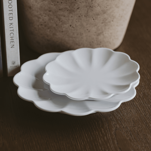 Two white melamine trays with scalloped edges stacked on a wooden surface.