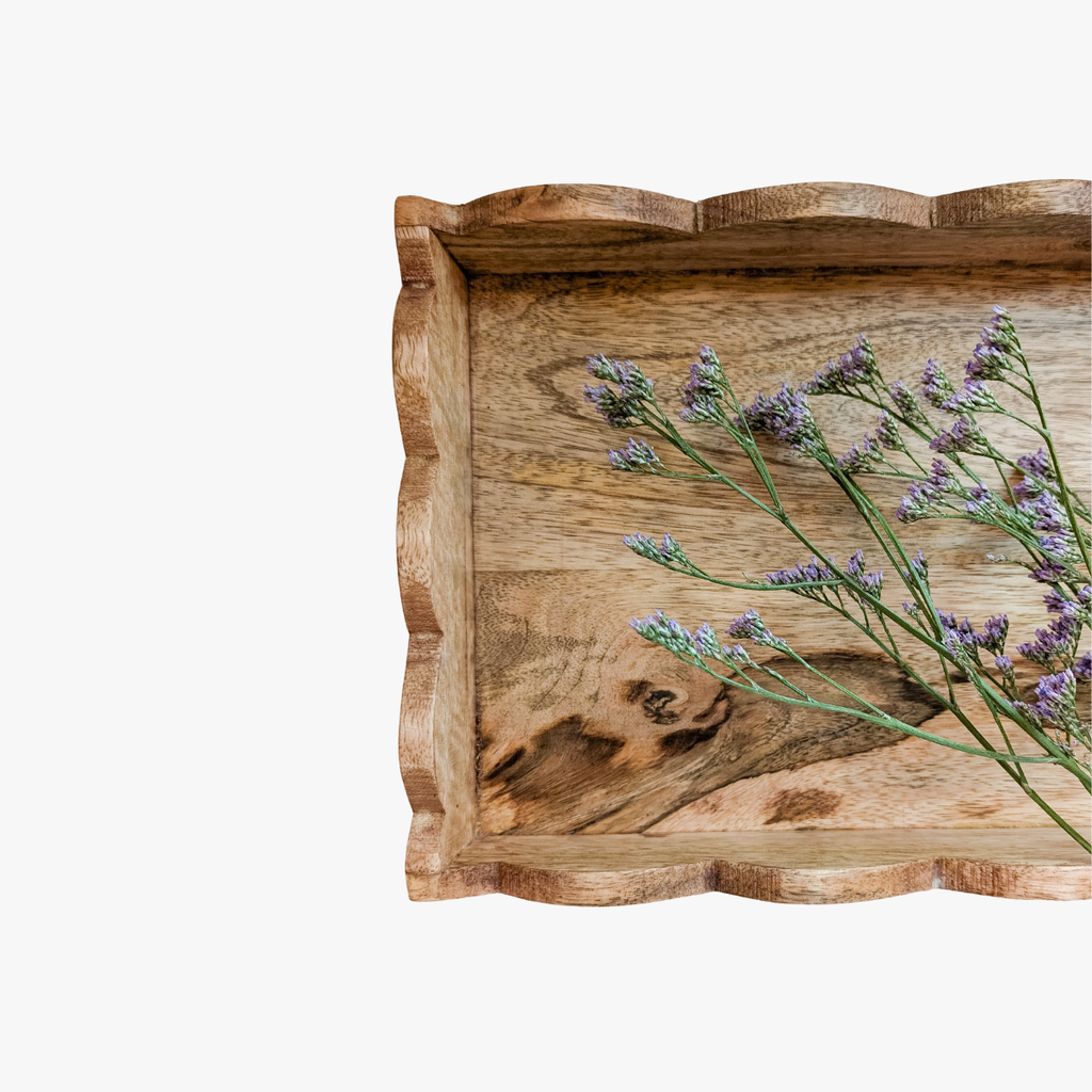 Wooden tray with wavy edge holding lavender flowers on a white background