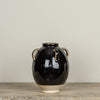 Black ceramic vase with beige accents on a wooden surface against a plain background