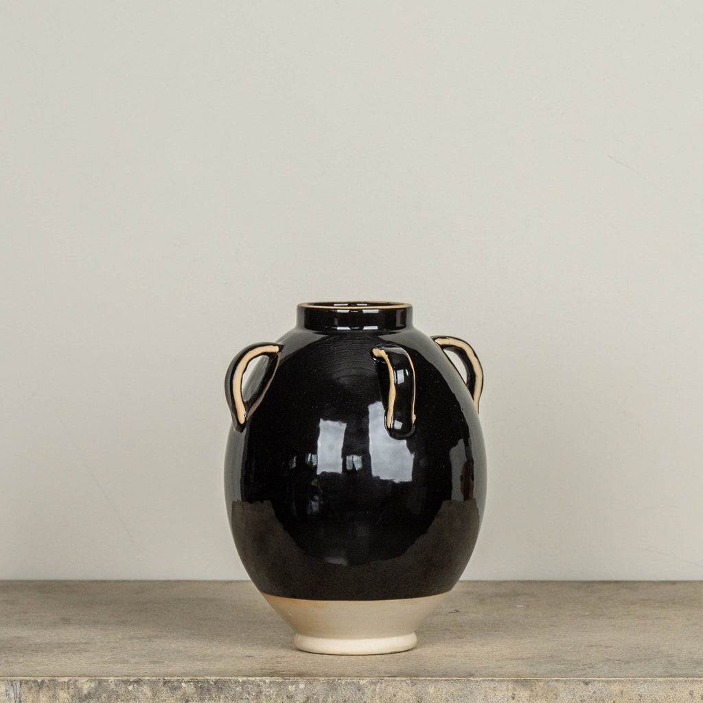 Black ceramic vase with beige accents on a wooden surface against a plain background