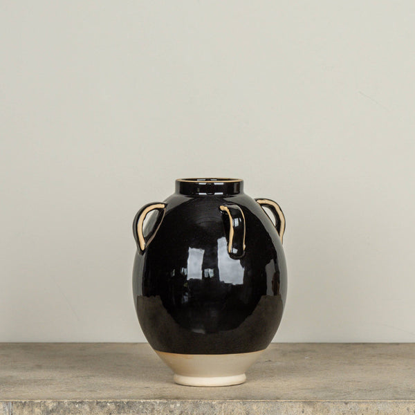 Black ceramic vase with beige accents on a wooden surface against a plain background