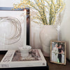 Decorative setup with a vase of yellow flowers, a book titled 'Still', and a framed photo on a surface.
