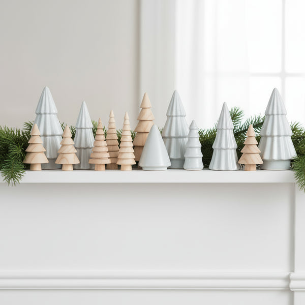Set of wooden and ceramic Christmas tree figurines on a white mantle with green garland. 