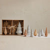 Set of wooden and stoneware Christmas trees in a box with decorative straw on a beige background