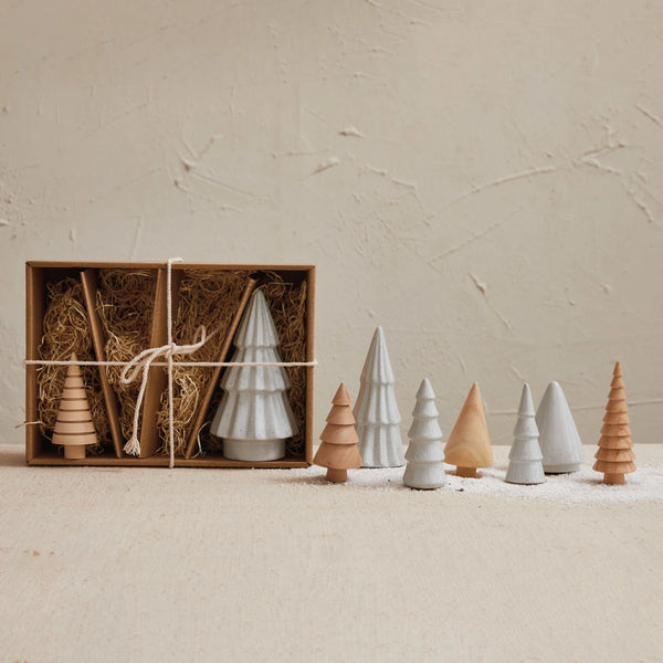 Set of wooden and stoneware Christmas trees in a box with decorative straw on a beige background