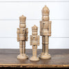 Three wooden nutcracker figurines on a wooden surface with a white wooden panel background.