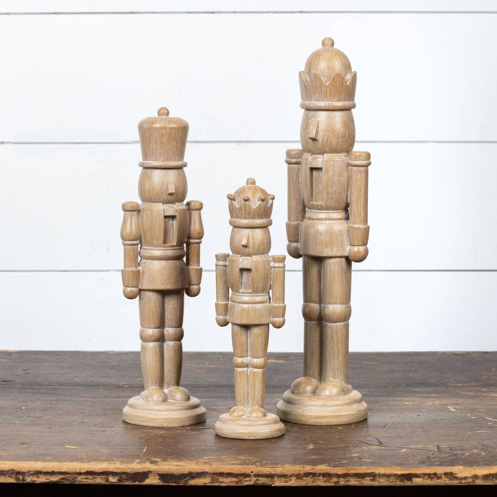 Three wooden nutcracker figurines on a wooden surface with a white wooden panel background.