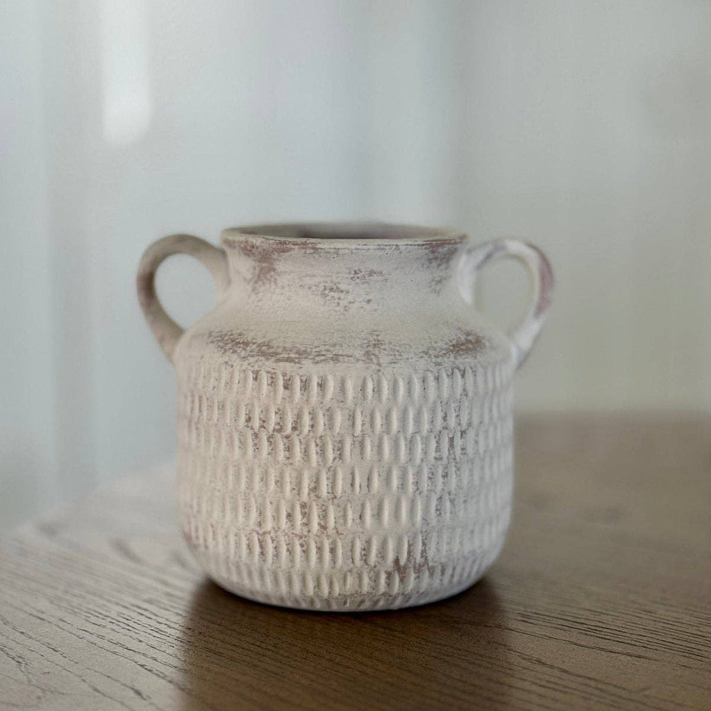 White textured ceramic vase with two handles on a wooden surface.