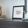 Framed artwork on a shelf with decorative items