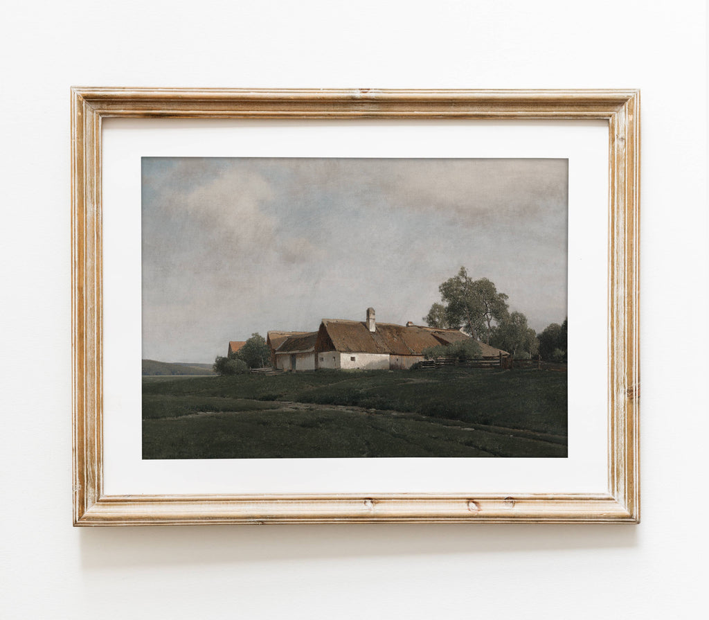 A framed landscape art print depicting a small farmhouse with a brown roof on a grassy hill under a cloudy sky, enclosed in a distressed light wood frame with a white mat.