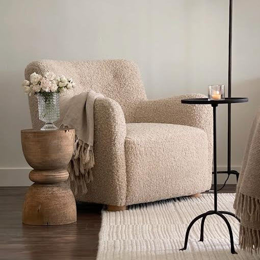 Beige armchair in a living room with a wooden side table and floor lamp.