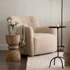 Beige armchair in a living room with a wooden side table and floor lamp.