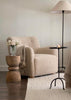 Beige armchair in a living room with a wooden side table and floor lamp.