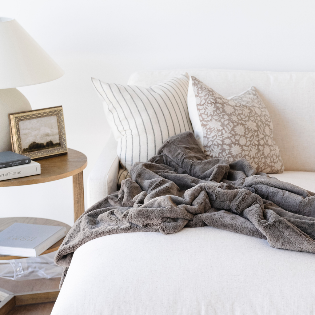 Gray blanket draped over a white sofa with decorative pillows in a cozy living room setting.